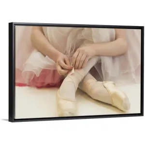 "A ballerina sitting on the floor tying her ballet shoes" Black Float Frame Canvas Art