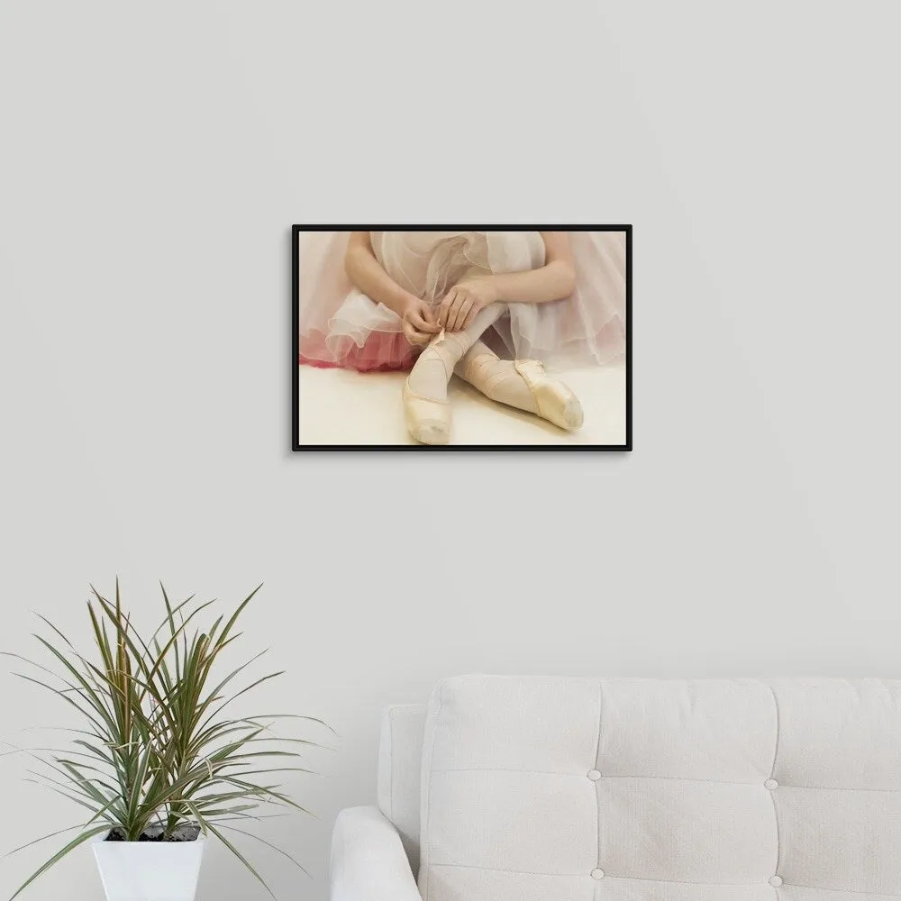 "A ballerina sitting on the floor tying her ballet shoes" Black Float Frame Canvas Art